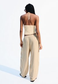 Beige gestreiftes Zweiteiler-Set mit einem trägerlosen Cropped Top und weitgeschnittenen Hosen mit elastischem Bund. Weicher Stoff und lässige Passform.
