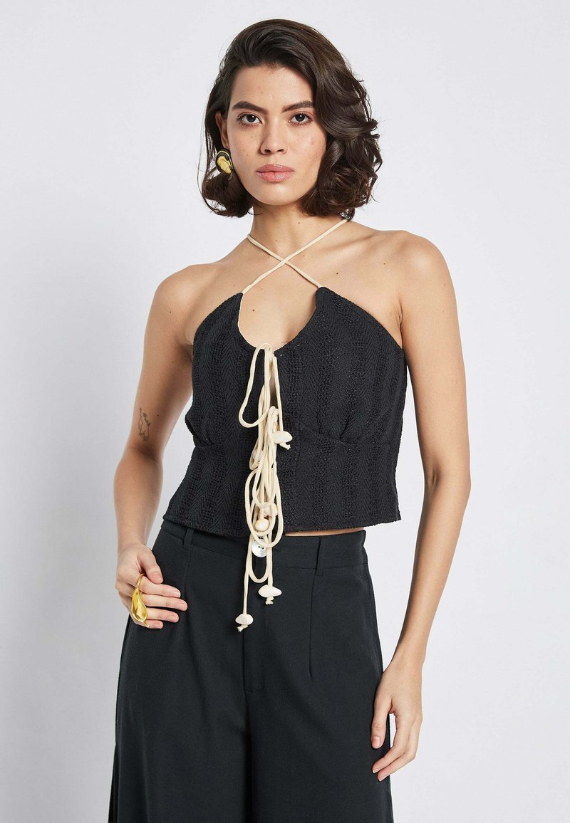 Top nero corto con un motivo testurizzato, caratterizzato da un design a collare halter e lacci crema con perline decorative sul davanti.