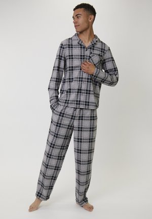 Hombre de pie descalzo, vistiendo una camisa de pijama de manga larga a rayas en tonos gris y negro con botones y pantalones de pijama a juego.