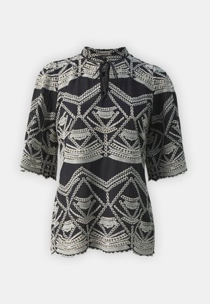 Blouse noire avec une broderie géométrique argentée complexe, col haut, manches courtes et ourlet festonné. Tissu texturé.