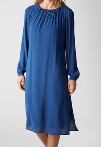 Abito lungo a maniche lunghe di colore blu scuro con scollo arricciato, texture liscia, lunghezza al ginocchio e spacco laterale per facilitare i movimenti.