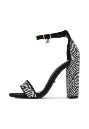 Sandalia de tacón en blanco y negro con un patrón geométrico, textura de ante, correa en el tobillo con hebilla dorada y diseño de tacón ancho.