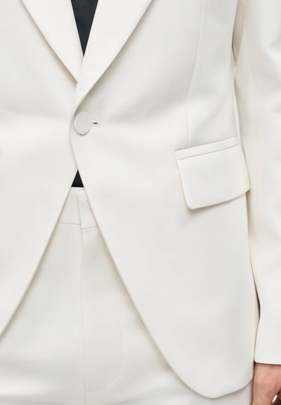 Κοντινή λήψη λευκού καλοραμμένου σακακιού και ταιριαστού παντελονιού, με ένα κουμπί κουμπωμένο και τσέπη με πτερύγιο στο μπροστινό μέρος του σακακιού.