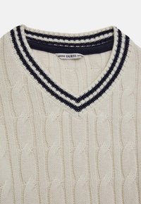 Gilet in maglia a coste color crema con scollo a V e colletto a righe blu navy e bianche. L'etichetta riporta "GUESS" sulla parte interna del collo.