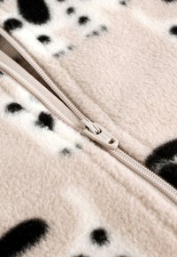 Beige színű gyapjú anyag fekete és fehér pöttyös mintával; jellemzője egy világos bézs cipzár texturált húzóka szerkezettel.