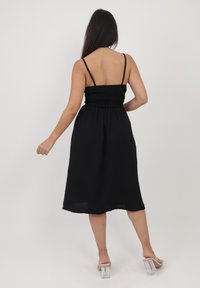 Vestito nero di lunghezza media con spalline sottili e corpetto arricciato. Tessuto testurizzato con una gonna fluida. Indossato con scarpe con tacco a blocco trasparente.