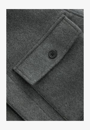 Szary wełniany płaszcz z teksturowanym wykończeniem, prostokątną kieszenią z czarnym guzikiem oraz widocznymi detalami szwów.
