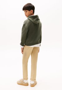 Oliven grøn hætte sweatshirt, lyse khaki bukser, beige sneakers med hvide accenter. Har en afslappet pasform og bløde teksturer.
