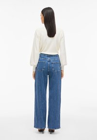 Μπλε τζιν με φαρδύ πόδι και ψηλή μέση, με δύο πίσω τσέπες, σε συνδυασμό με κρεμ μπλούζα μακριού μανικιού. Λείος υφασμάτινος ιστός; casual σχέδιο.