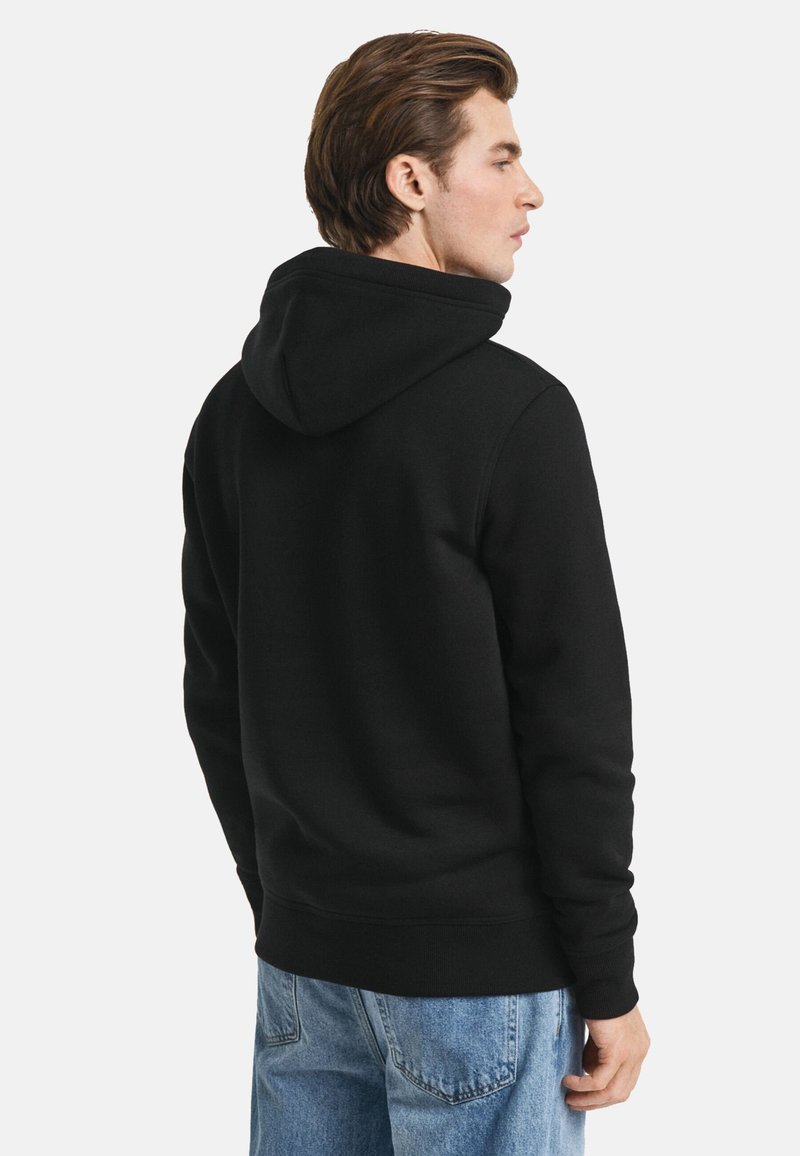 Svart hoodietröja med stor huva, ribbade ärmslut och nederkant, tillverkad av mjukt tyg. Stylad med ljusblå jeans som visar en avslappnad design.