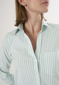 Camicia a righe verde chiaro e bianca realizzata in tessuto morbido, con chiusura a bottoni sul davanti, colletto e una tasca sul petto.