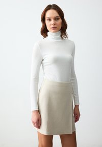 Witte geribde coltrui gecombineerd met een beige suède mini-jurk, voorzien van een ritsdetail aan de zijkant en een soepele textuur.