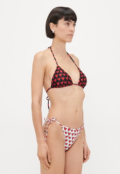 Bikini med svart topp med røde hjerte mønster og tynne stropper, kombinert med hvite truser dekorert med røde hjerter og knyting i sidene.