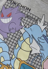 Grafisches T-Shirt mit Cartoon-Pokémon-Charakteren: Gengar (lila), Gyarados (blau), auf einem grauen Hintergrund mit Gittermuster und Text.