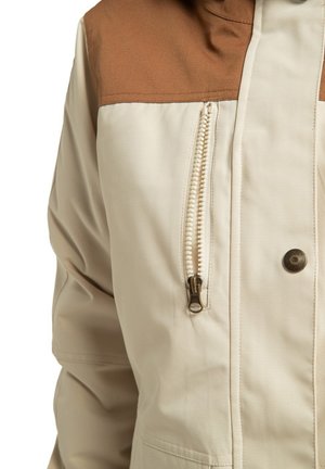 Beige jas met bruine schouderaccenten, voorzien van een zijzak met metalen rits en een knoopsluiting. Soepele textuur, casual ontwerp.