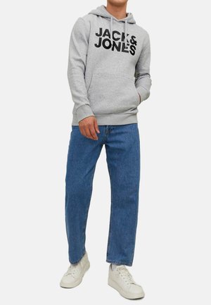 Grauer Kapuzenpullover mit schwarzem Logo-Text, kombiniert mit hellblauen, geraden Jeans und weißen Turnschuhen. Der Pullover hat eine Kängurutasche und eine Kordelzugkapuze.