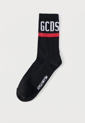 Black ribbed sock with white "GCDS" lettering near the top and a red stripe below, with small white text on the foot reading "MADE ITALY."