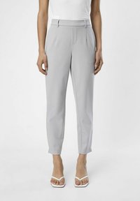Pantalons taillés gris avec une coupe droite, présentant un devant plat, des poches latérales et une texture lisse. Portés avec des sandales blanches à brides.