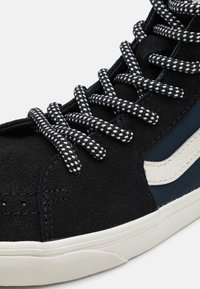 Zwarte hoge sneaker van suède met getextureerde marineblauwe meshpanelen, witte leren accenten en zwart-wit geruite veter.