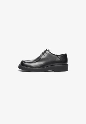 Chaussures en cuir noir avec un bout rond, des accents de couture droite et une semelle en caoutchouc à profil bas. Design classique et épuré, fermeture à lacets.