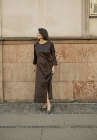 Brun satin klänning med båthals och trekvartsärmar, med en sidöppning och rynkad detalj. I kombination med svart-vita randiga klackar.