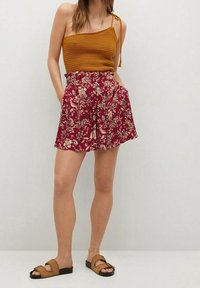 Haut court en maille jaune moutarde à fines bretelles, associé à un short imprimé floral bordeaux. L'ensemble est complété par des sandales marron à enfiler.