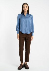 Jasnoniebieska satynowa koszula na guziki z kołnierzykiem, w zestawieniu z brązowymi dopasowanymi spodniami i ciemnobrązowymi butami typu slip-on. Gładka tekstura i dopasowany krój.