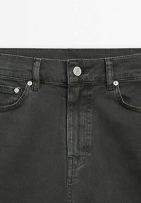 Gros plan sur la zone de la taille d'un jean en denim gris foncé avec bouton à l'avant, passants de ceinture et deux poches avant avec rivets.