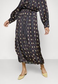 Maxihame, jossa on monivärinen geometrinen kuvio, joustava vyötärö, sileä pinta ja lentävä muotoilu, yhdistettynä keltaisiin matalakorkoisiin kenkiin.