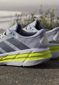 Zapatillas deportivas grises con parte superior texturizada, acentos en amarillo neón y un diseño de suela distintivo que presenta la etiqueta "REPETITOR".