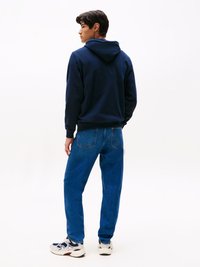 Felpa navy con cappuccio e cordino, abbinata a jeans blu a gamba dritta e sneakers bianche, vista da dietro.