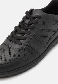 Sneaker in pelle nera forata con pannelli testurizzati, lacci neri piatti e un branding discreto su un lato. Suola in gomma per una migliore aderenza.