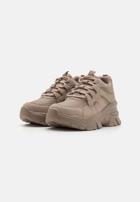 Zapatillas beige con una parte superior de tela texturizada, que cuentan con una suela gruesa y acolchada, punta redondeada y un sistema de cordones prominente.