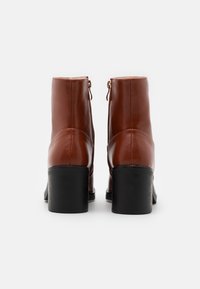 Bottes cheville en cuir marron avec une texture lisse, talon bloc et fermeture éclair latérale. Couture renforcée le long des coutures.