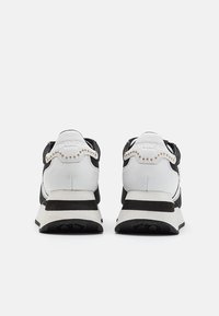 Paire de baskets à plateforme noires et blanches avec des détails de clous dorés sur les languettes du talon, vues de dos sur un fond blanc.