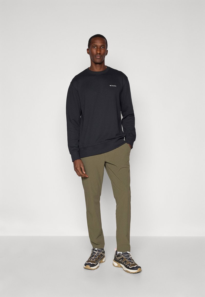 Sweatshirt noir à manches longues avec des manches à revers, pantalon tapered vert olive, et baskets noires et grises avec une semelle beige et des détails de lacets.