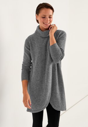 Grå, stickad tunika med hög ribbad krage, långa ärmar och en rundad nederkant, tillverkad av mjukt, texturerat tyg. Matchad med svarta leggings.