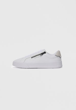 White low-top sneaker with side zipper and laces, beige heel tab, and "Tommy Hilfiger" logo on the side.
