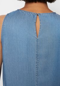 Blå denim ermeløs topp med en nøkkelhullåpning bak, synlig søm og myk tekstur. Avslappet design.