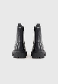 Par de botines de cuero negro con suelas gruesas acanaladas y cremallera lateral vistos desde la parte trasera sobre un fondo liso.