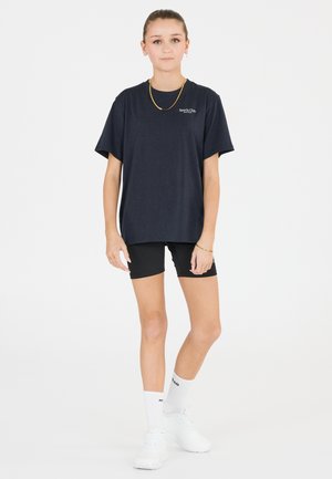 Marinblå bomulls-T-shirt med avslappnad passform, korta ärmar och en liten logotyp. Matchas med svarta shorts, vita sneakers och mönstrade strumpor.