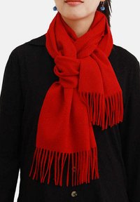 Sciarpa di lana rossa con frange, drappeggiata elegantemente attorno al collo, che completa un top nero. Texture morbida e colore uniforme.