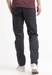 Marinblå lätta byxor med slim fit, som har sidofickor och en detaljerad knapp, kombinerat med vita sneakers.