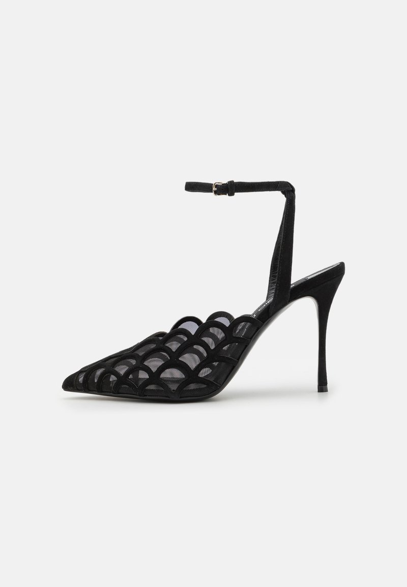 Sandale noire à talon avec un nez pointu, présentant un design en maille ouverte, une texture en daim et une sangle de cheville avec un détail de boucle.