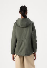 Veste à capuche vert olive avec une coupe décontractée, des détails de couture visibles et des poches avant. Tissu doux au toucher lisse.