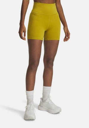 Gele high-waisted shorts met een gladde textuur, zijzakken en contrasterende stiksels, gecombineerd met witte sportschoenen en sokken.