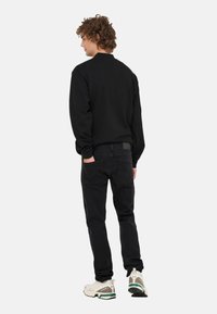 Czarna bluza z długimi rękawami, zestawiona z czarnymi dżinsami. Model nosi białe trampki z zielonymi akcentami, widziany od tyłu.