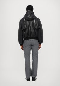 Doudoune noire et brillante avec capuche, dotée de deux poches zippées à l'arrière. Associée à un jean droit gris et des chaussures noires.