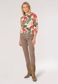 Maglione multicolore con motivo astratto in rosso, verde e beige, abbinato a pantaloni a quadri beige e marroni. Stivaletti con tacco in suede beige.