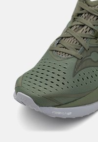 Baskets de sport vertes avec une tige en maille, trous de ventilation visibles, semelle en caoutchouc et accents texturés. Comprend des lacets plats et un détail de logo.
